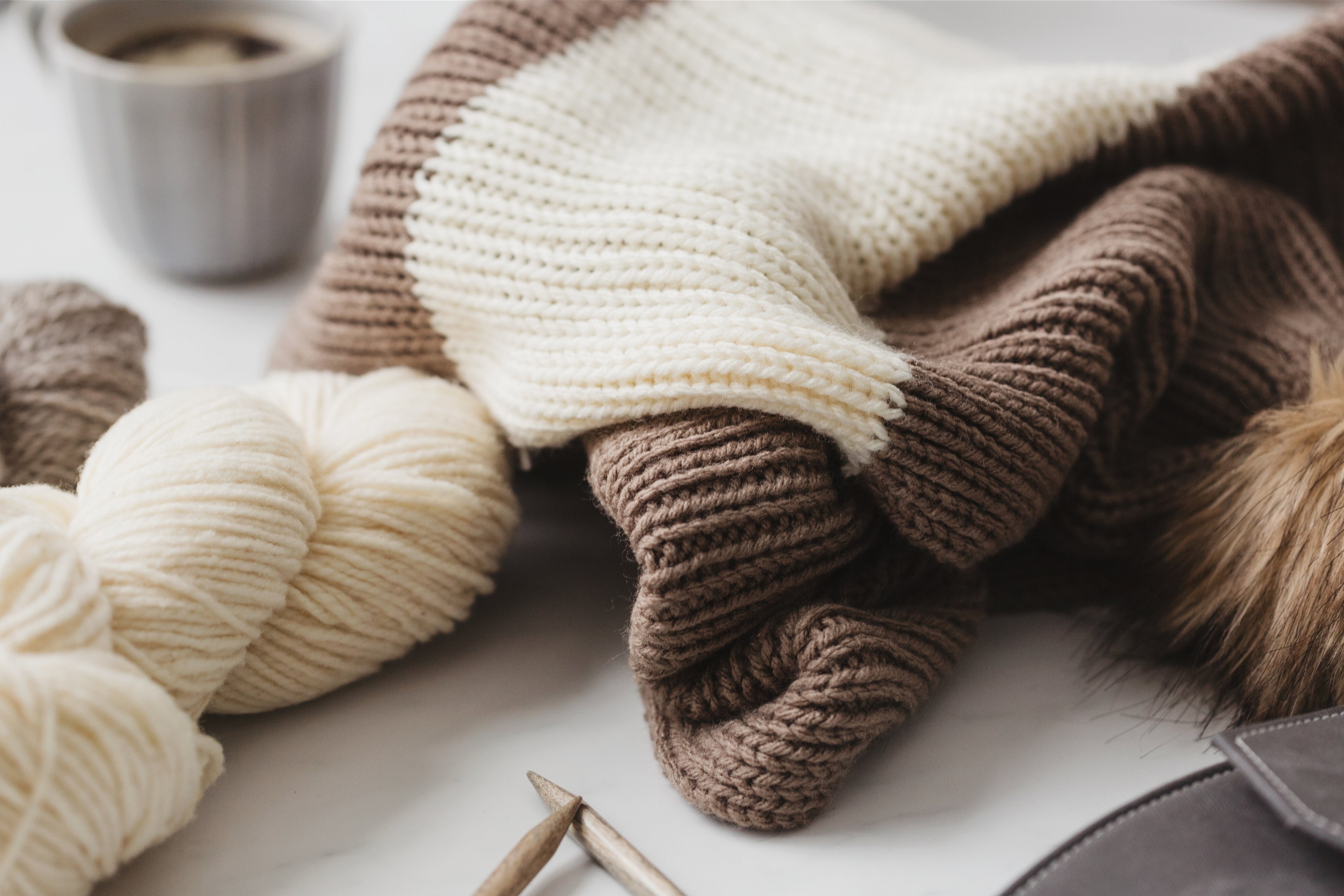 cream and brown knitting, cream skein of yarn, with coffee and knitting needles peeking in